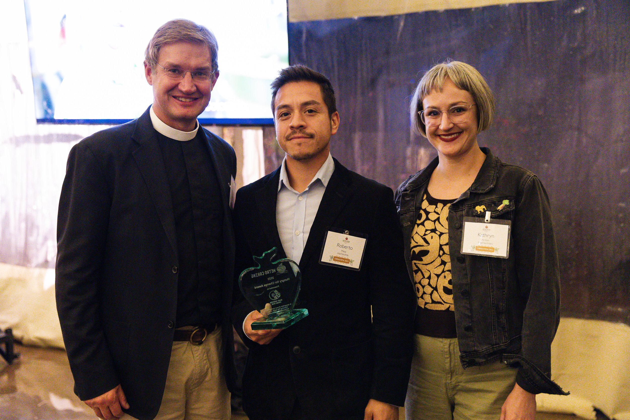 Reverand Richard Lawson from St. John’s Cathedral presents the 2023 Metro Caring Hungry for Change Award to East Denver Food Hub’s co-founder Roberto Meza and Food Hub Director Kathryn Ardoin at Cornucopia 2023.