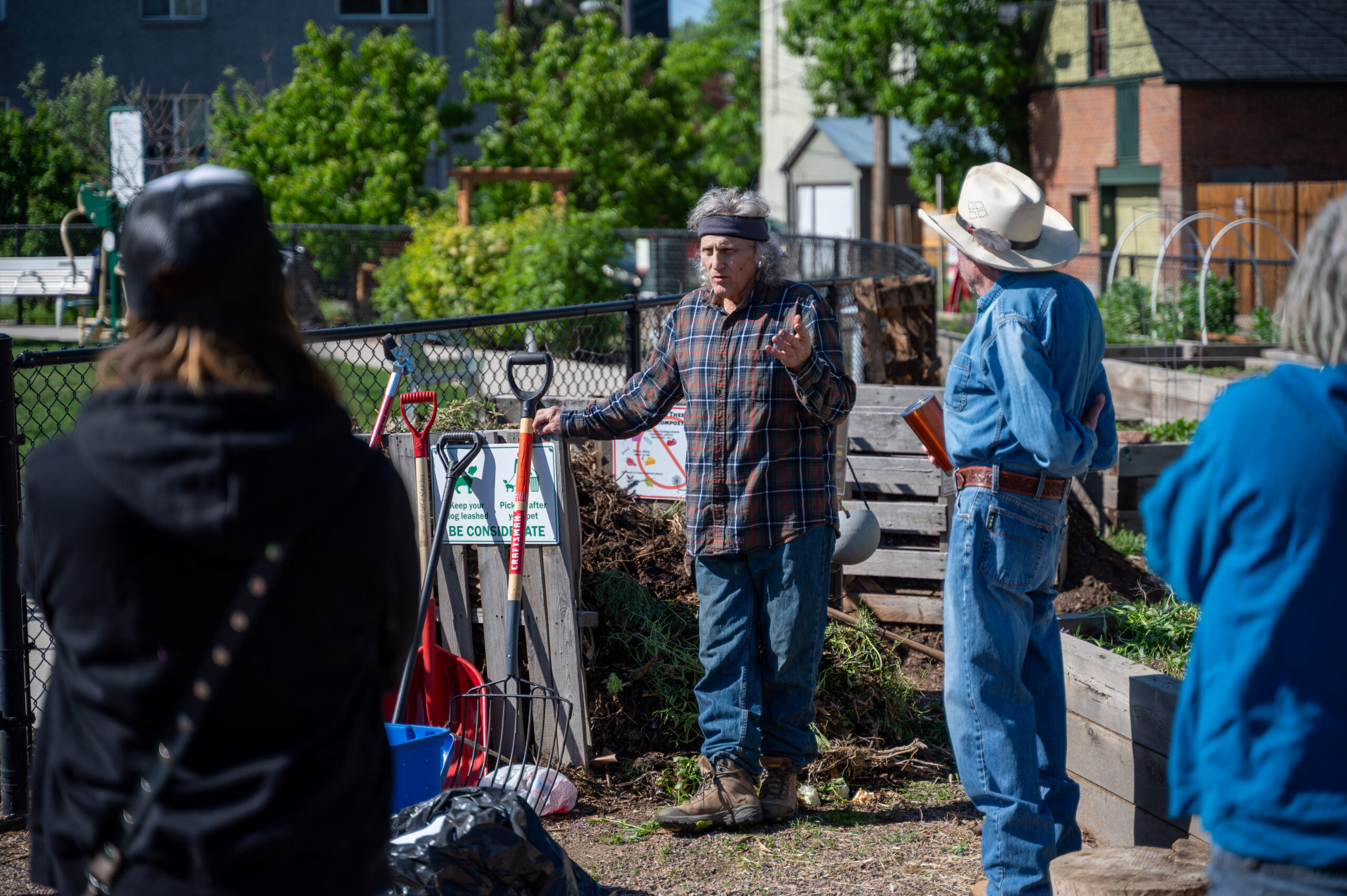 Community gardeners gather around one gardener who is talking and explaining things about compost.