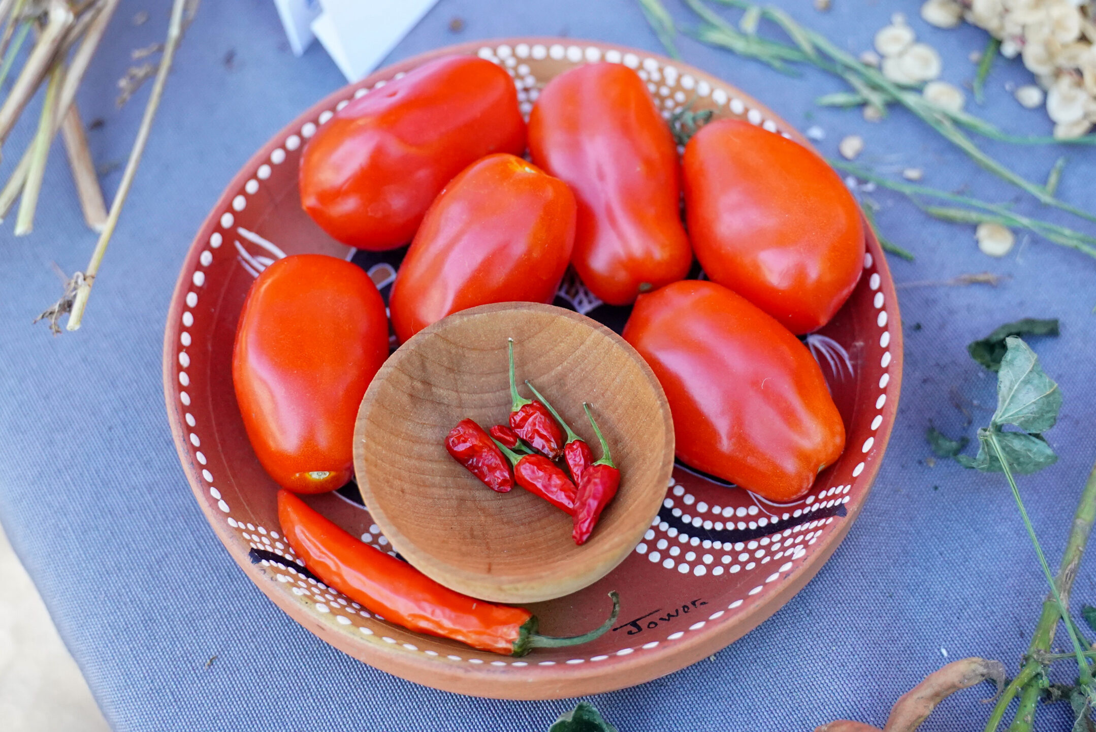 A small bowl with red chile peppers sits inside a larger bowl that's filled with roma tomatoes.