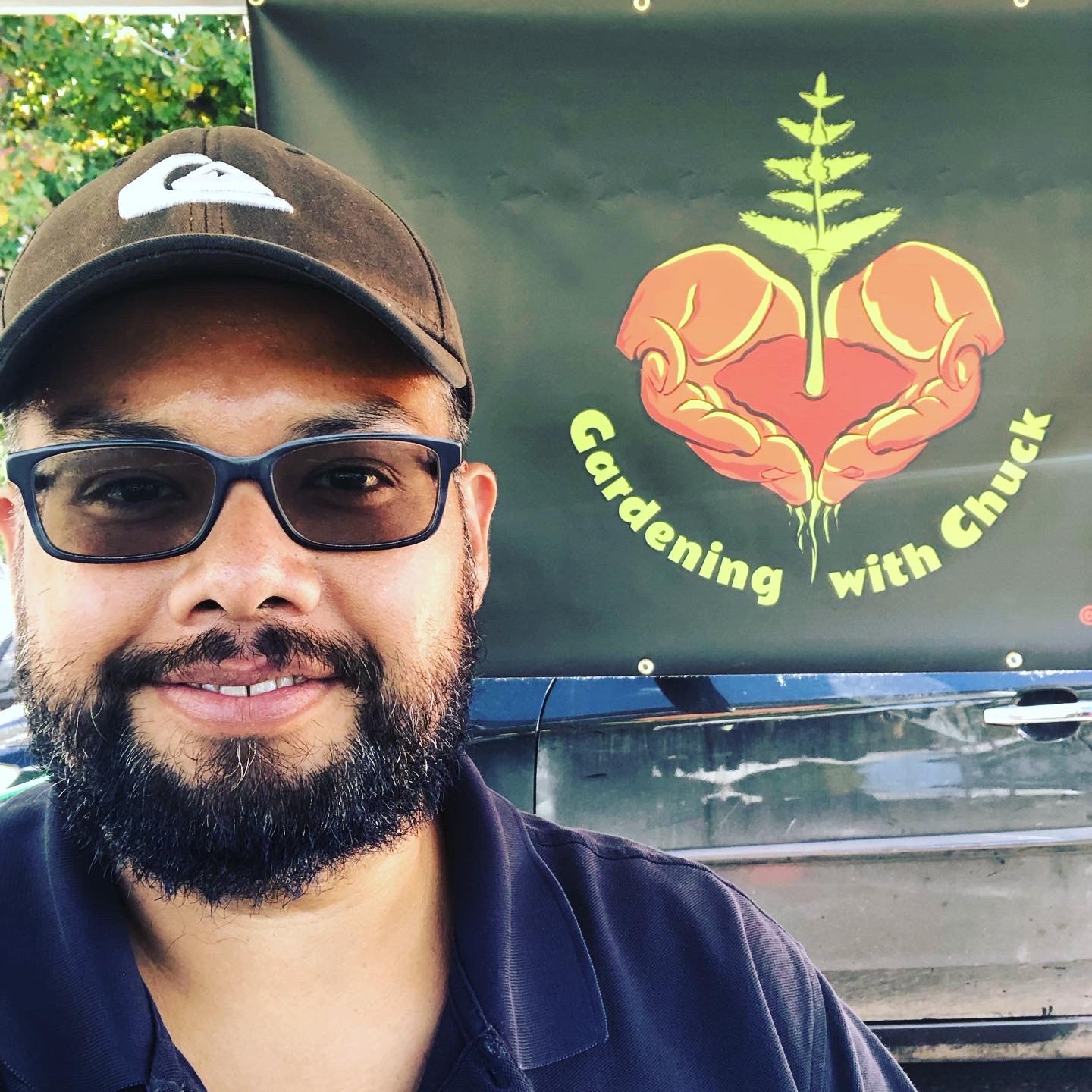 Chuck takes a selfie with his logo behind him at his farmer's market stand. 