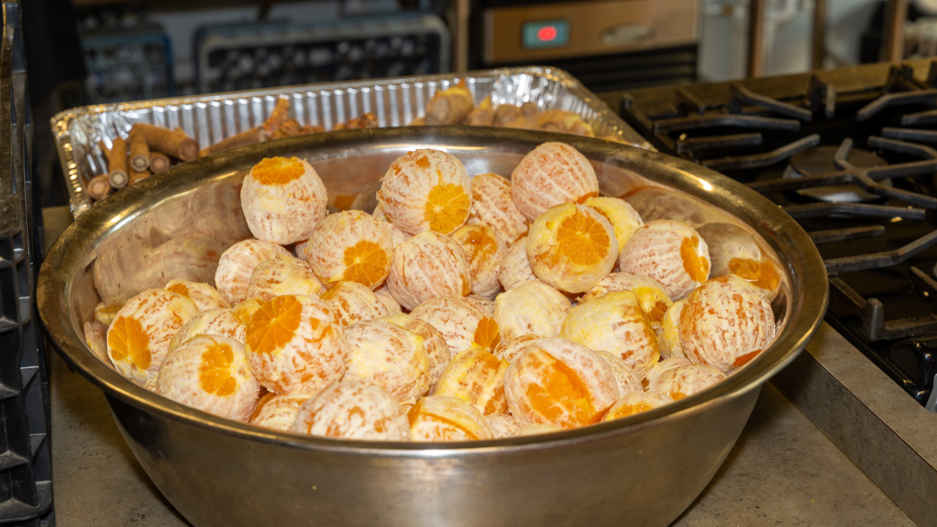 Large bowl of dozens of peeled oranges. A tray of ginger root is behind it.