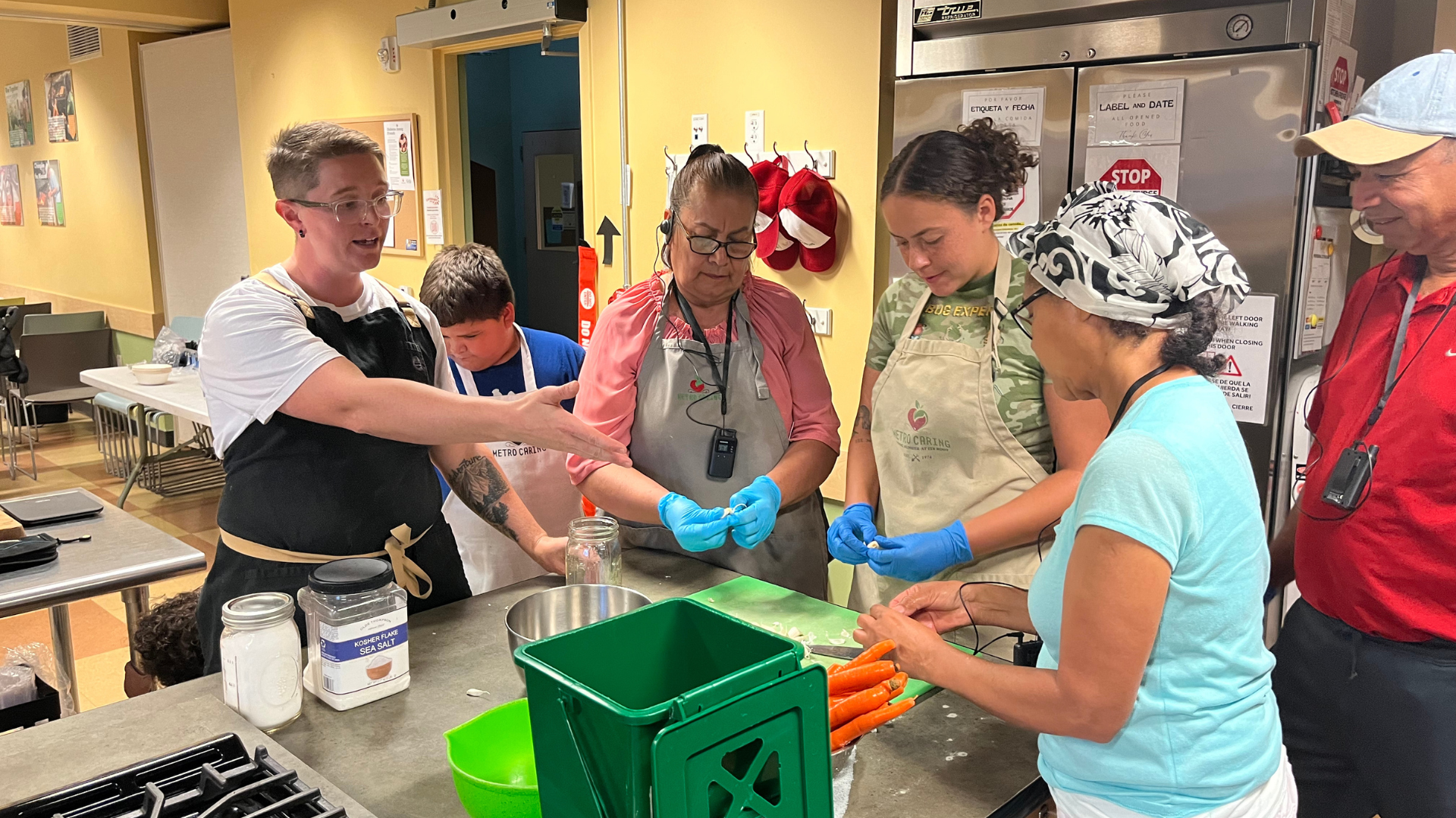 Multiple people gather around the kitchen counter to chop carrots and ferment them.