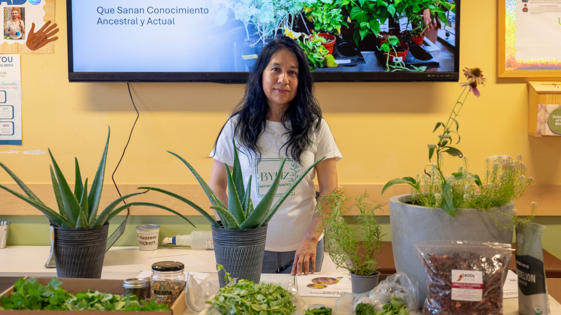 Elizabeth stands behind a table of plants, prepared to present her Medicinal Plants workshop.