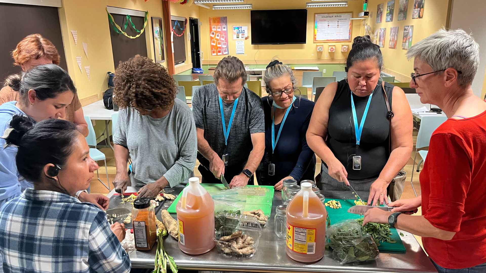 Class attendees gather around the Metro Caring kitchen prep table to chop ginger and other herbs.