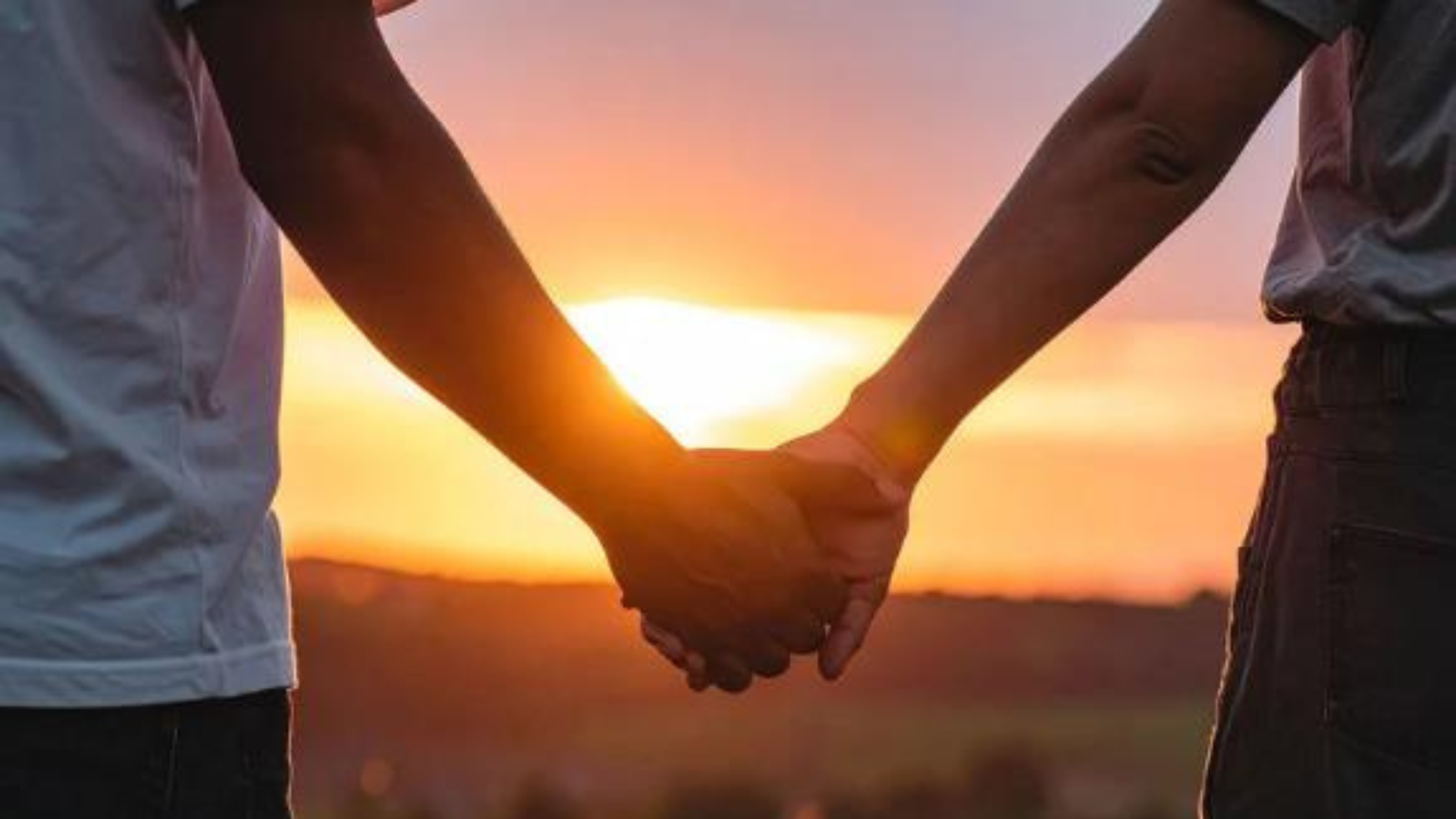 Two people hold hands while the sun sets in the background.