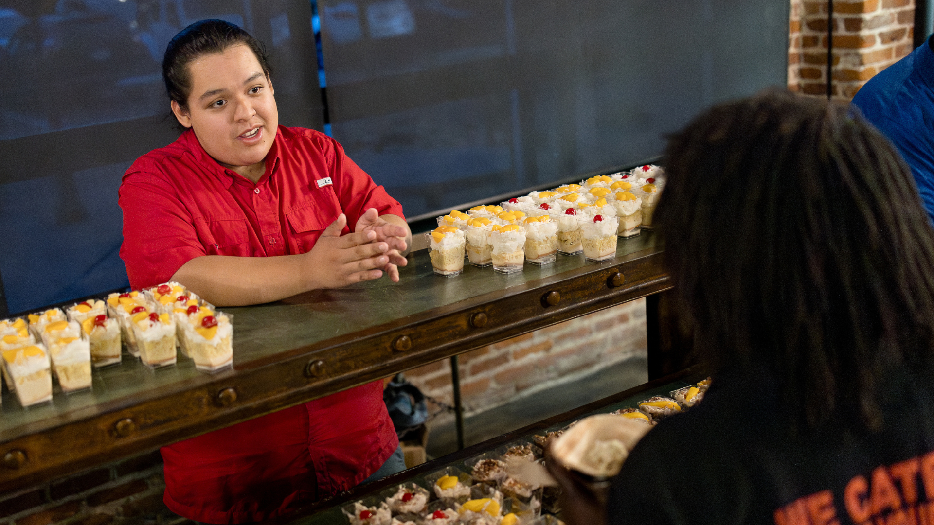 Caterer shares about dessert options with guest. Small cups with various desserts line the table.