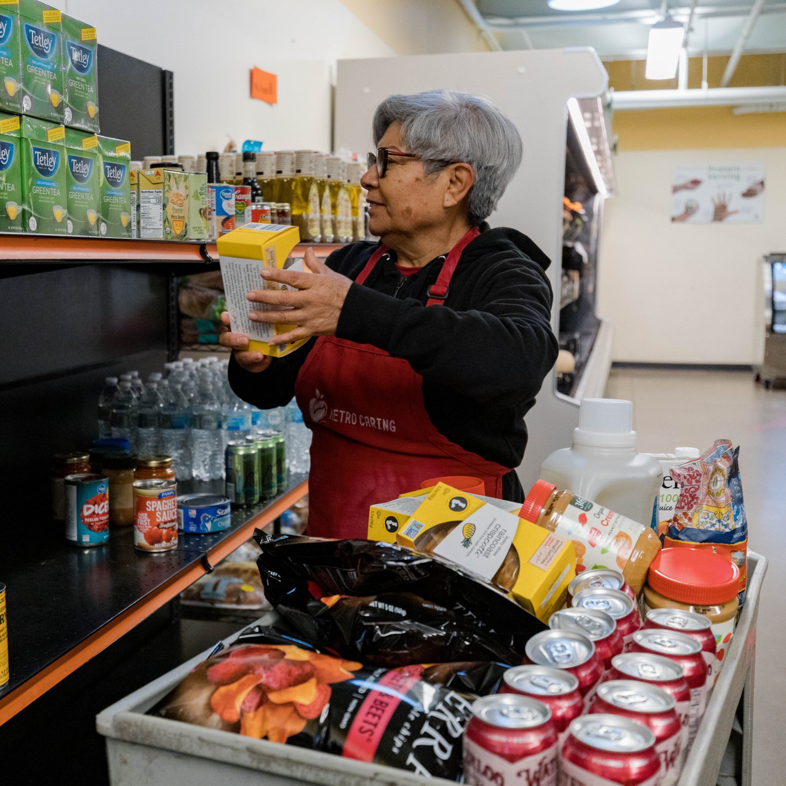 Rosa stocks shelves in the Fresh Foods Market, wearing a red Metro Caring apron.