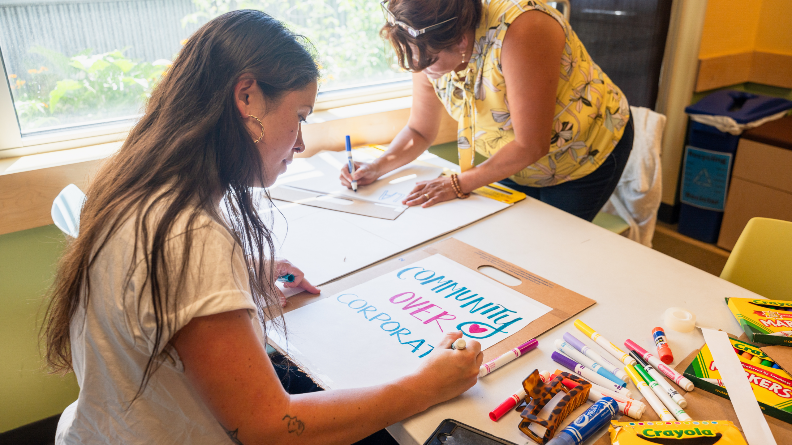 Two women sitting on a table and drawing on a paper during a community workshop